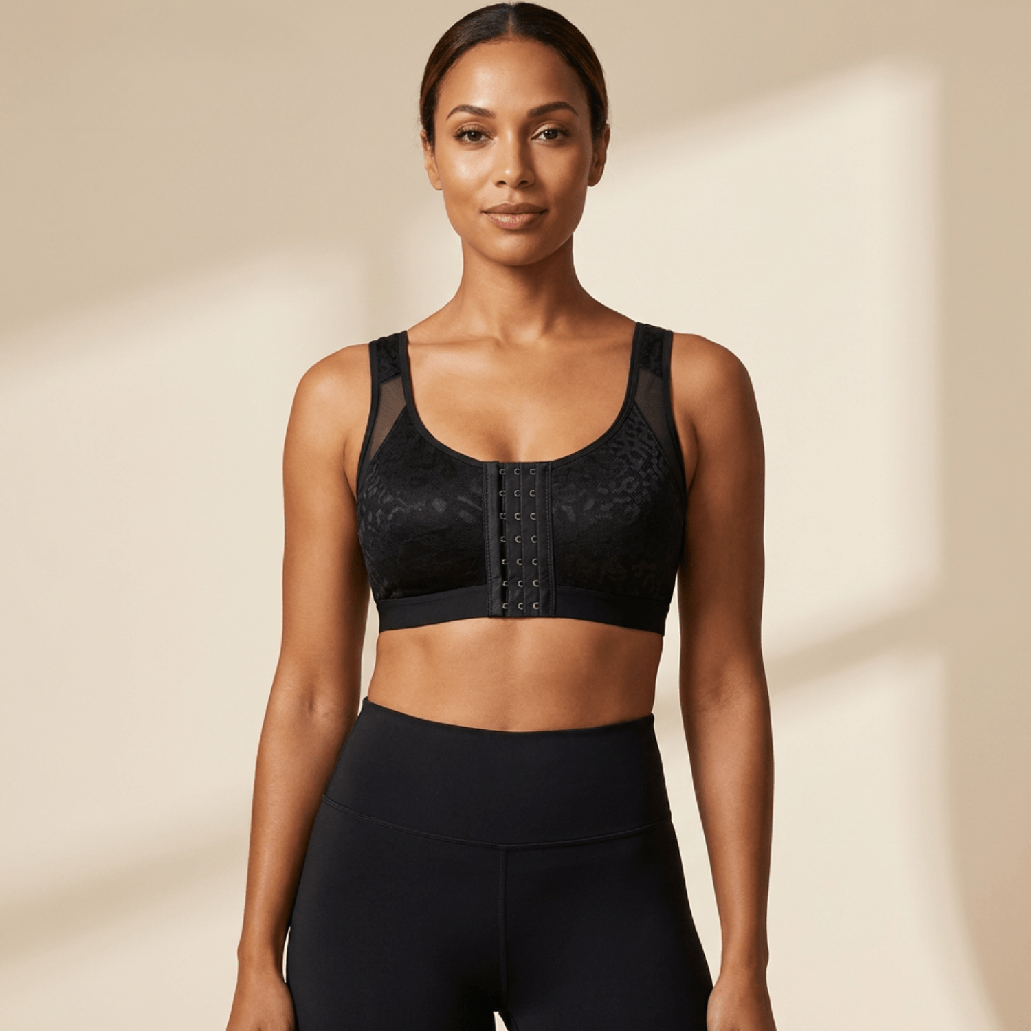 Brassière sport femme maintien fort noir avec motif délicat, vue de face, studio minimaliste ivoire, legging noir, pose fashion glam chic